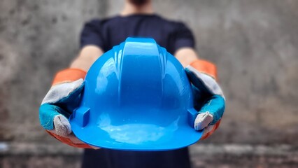 Construction worker offering a blue hard hat for safety and protection on the job