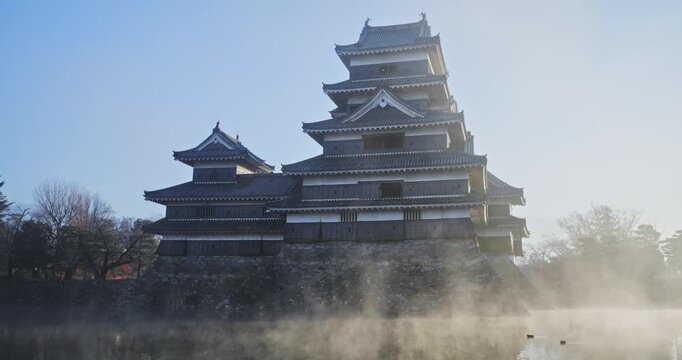 Morning mist rising from pond to silhouetted 16th century Matsumoto castle at sunrise