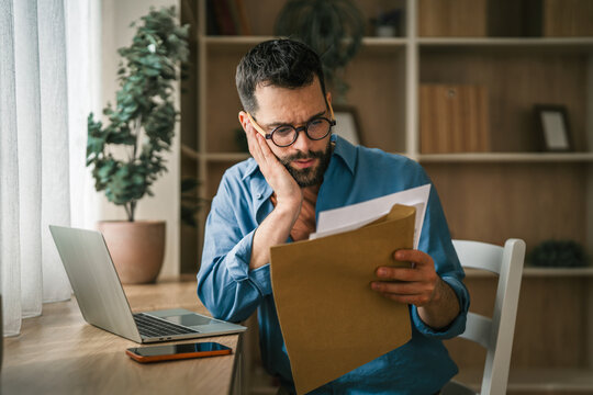 Worried man calculating finances with paperwork and laptop