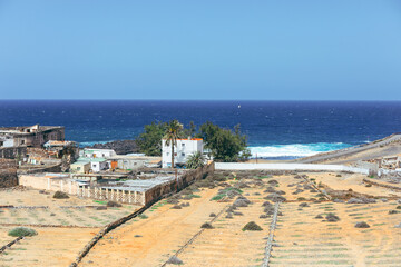 Small whitewashed houses sit between an arid, volcanic landscape and the deep blue Atlantic in gran canaria. Coastal scene captures rustic atmosphere of the Canary Islands under a clear sky