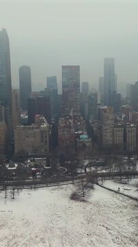 Aerial view of Central Park snowy meadow with Manhattan skyscrapers under foggy overcast sky