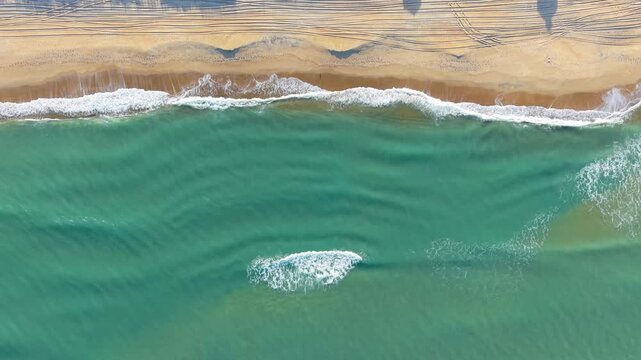Kill Devil Hills, North Carolina, a top-down aerial view of turquoise Atlantic waters crashing against a sandy beach shoreline with tire tracks on the Outer Banks.