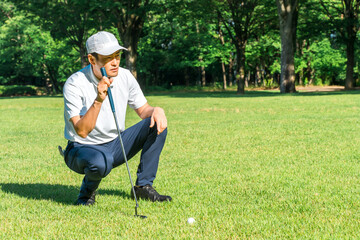 Fototapeta premium Male golfer reading the line on the golf course green
