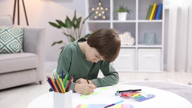 Little boy drawing with brown felt pen at white table indoors, camera moving down
