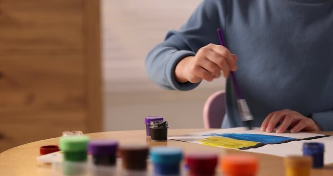 Little girl drawing with brush and paints at table indoors, closeup. Camera moving left