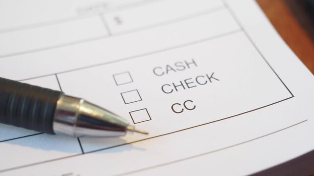 Macro close up of pen moving toward payment method check box on receipt pad in restaurant