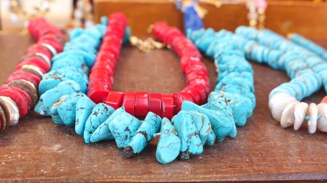 Cinematic close up of vibrant turquoise and coral bead necklaces on wooden display