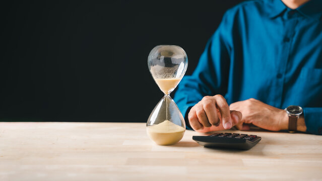 Hourglass sand flowing, tax payment deadline approaching, business person calculates corporate income money for year end, strategic financial planning crucial to save funds
