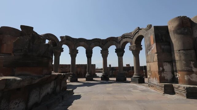 Explore the ancient ruins of Zvartnots Cathedral in Armenia. This beautiful historical site features stunning stone pillars and arches under a clear blue sky, showcasing remarkable medieval architectu