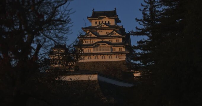 Sunset glow on ancient 16th century Matsumoto castle with silhouetted trees - locked off shot