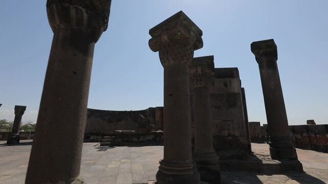 Explore the ancient ruins of Zvartnots Cathedral in Armenia. This beautiful historical site features stunning stone pillars and arches under a clear blue sky, showcasing remarkable medieval architectu