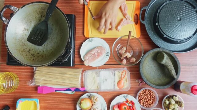 Top view of person cutting raw chicken breast into cubes on an orange board for Indonesian satay