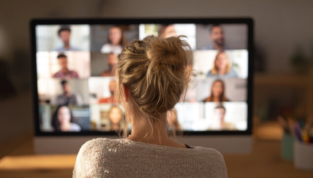 Woman watching an online video conference call on a computer, with multiple participants visible on the screen.
