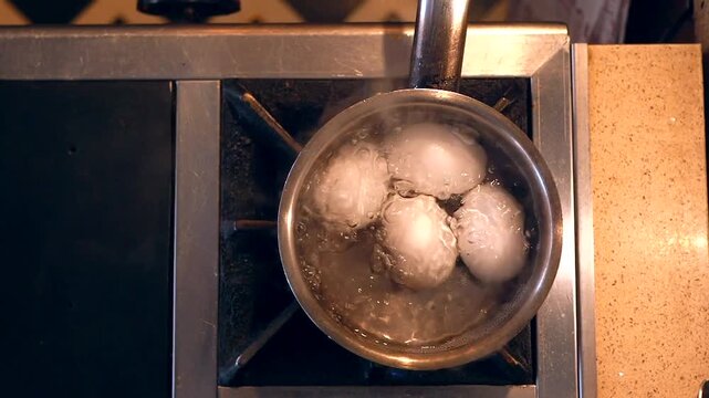 Top view of white eggs boiling in stainless steel pot on gas stove with bubbling water