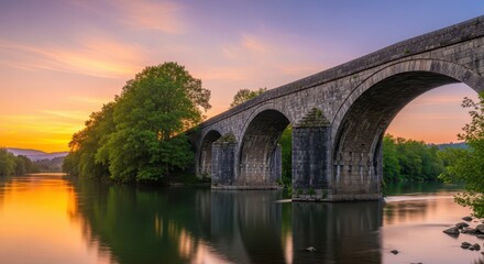 Fototapeta premium Ancient stone aqueduct spans calm river waters under a vibrant sunset sky