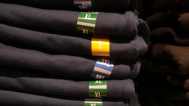 Stack of folded navy blue and brown cotton t shirts with size stickers in retail clothing store display