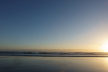 Obraz premium Sun rises in golden hour from right of frame over a calm sea and beach in Australia, Evans Head,