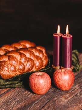 Challah bread with red apples and burning candles on a rustic wooden table for Rosh Hashanah Jewish New Year celebration festive greeting card layout with copy space