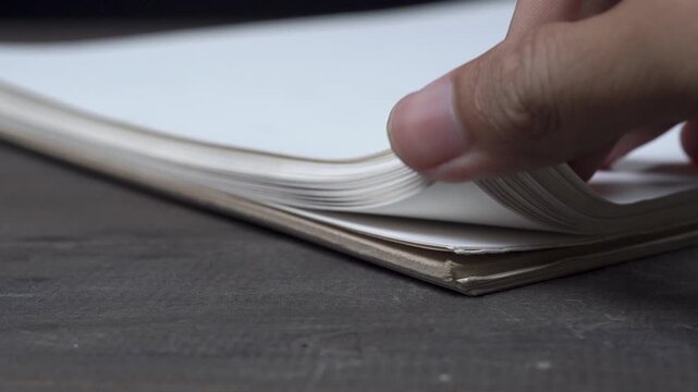 Close-up of hands opening a book, creating soft paper flutter
