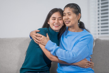Naklejka premium An elderly Asian woman daughter sit on a sofa embracing warmly, eyes closed and smiling, expressing deep love, gratitude, emotional support, and a strong multigenerational family bond at home