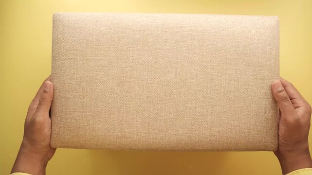 Hands opening and displaying large rectangular beige fabric storage box on yellow background