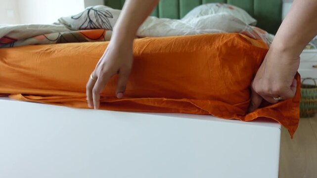 Person making bed with orange sheet for comfortable sleep, a cozy home bedroom setting
