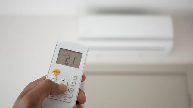 Person using air conditioner remote control to decrease room temperature in modern interior