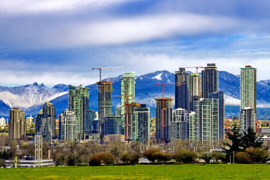 Residential area of high-rise buildings in the city of Burnaby, construction site in the center of the city against the backdrop of snow covered mountain range and cloudy sky