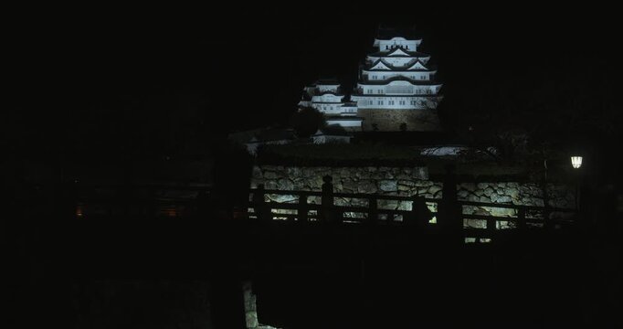 Silhouettes of people walking over bridge with view of ancient 16th century Matsumoto castle - wide shot