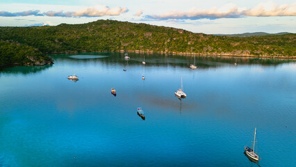 Aerial view of sailboats anchored in a calm turquoise bay surrounded by lush green hills © Hamid