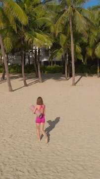 Fit Woman In Pink Activewear Walking On Beach Toward Palm Trees
