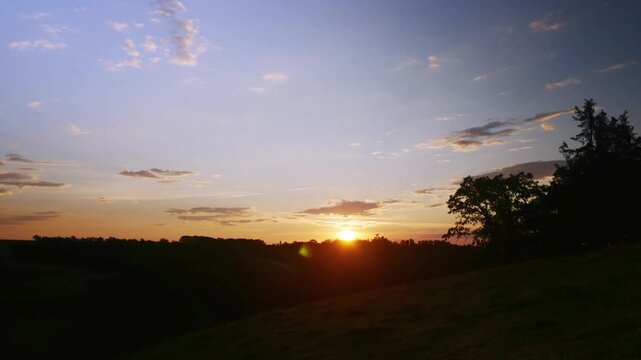 Time-lapse sunrise with zoom-back and tilt-down over silhouetted trees and open rural field.