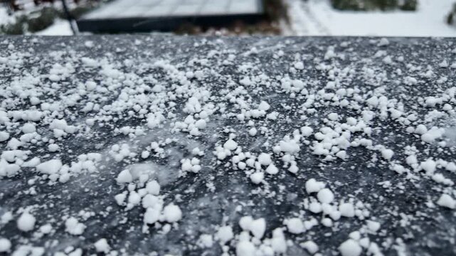 Macro close up of white graupel falling on dark granite surface during winter storm