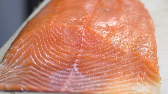 Close up video showing an uncooked fresh salmon fillet with its skin on a white cutting board, revealing intricate patterns of muscle and fat, ready for cooking or preparation
