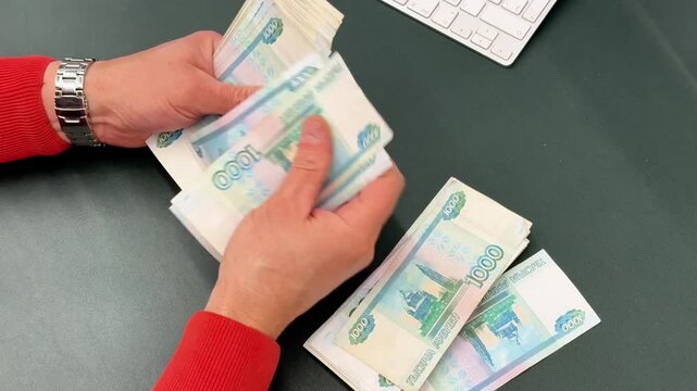Man counts a bundle of bills for one thousand Russian rubles at the workplace. Man counts paper, 1000 rubles bills. Russian cash money in male hand. A man holds a wad of money in his hands. Money. 