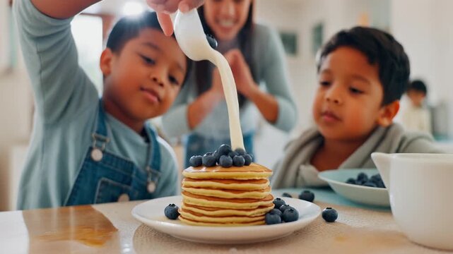 Morning Pancake Mess. Home Cooking & Family Bonding in the Kitchen. Family / Breakfast. two siblings competing to pour blueberries onto a stack of pancakes while a parent watches in the background
