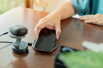 Fototapeta premium Woman placed smartphone on a wireless charger next to an earphones charging