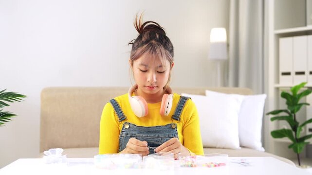 Bead arts. Inspired tween girl enjoy hobby make handmade fashion jewelry from colorful plastic beads set stringing beads on strips in living room at home.