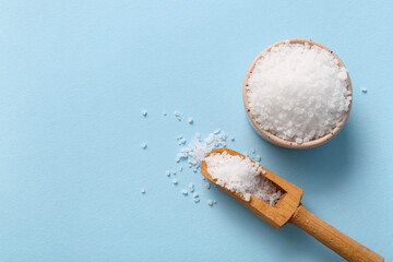 Wooden scoop and bowl with sea salt on color background