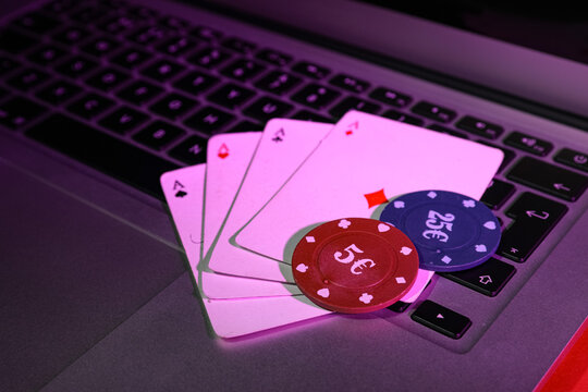 Laptop with playing cards and poker chips on red table, closeup