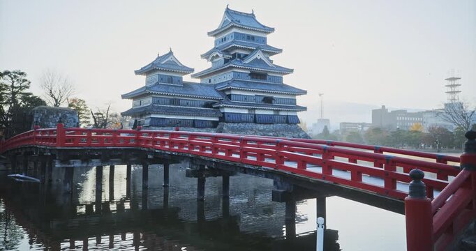 Cinematic view of Japanese bridge and silhouetted 16th century Matsumoto castle over rippling pond