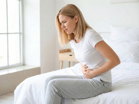 female experiencing stomach pain sitting on bed showing digestive health issue medical symptom and lifestyle healthcare awareness concept