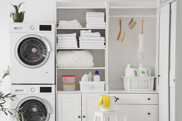 Interior of laundry room with washing machines, cleaning supplies and clean towels stacks in shelving units