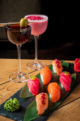 Vibrantly colored sushi elegantly arranged on wood, alongside chic cocktails in crystal glasses