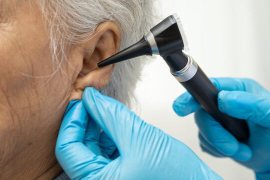 Otolaryngologist or ENT physician doctor examining senior patient ear with otoscope, hearing loss problem.