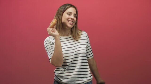 Woman holds glazed donut in hand with fist raised and mouth open while dancing in studio; joyful indulgence.