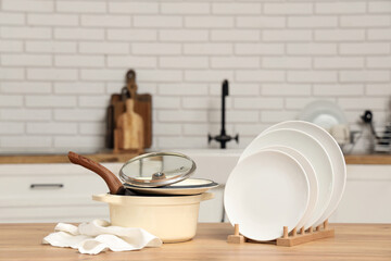 Clean plates, cooking pots and napkin on wooden table in kitchen