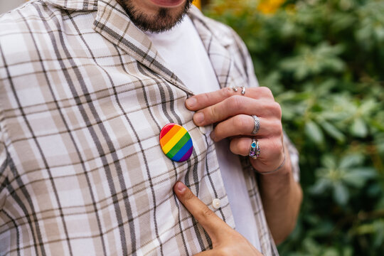 Person's hands adjusting a rainbow flag pin on a checkered shirt, symbolizing lgbtq plus identity, support, and diversity