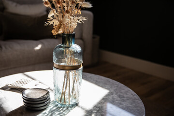 Sunlit glass vase with dried flowers on a modern living room table