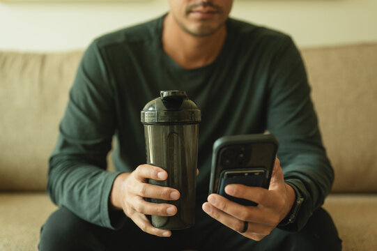 Young man holding protein shaker and tracking fitness on phone